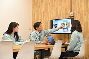 男性社員がモニターに写した内容を指さし女性社員に指示を出している写真